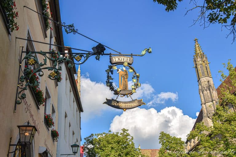 Letrero metálico del hotel Meistertrunk que representa al alcalde Nusch bebiéndose el gran vaso de vino con la torre de la iglesia de los franciscanos al fondo en Rothenburg ob der Tauber