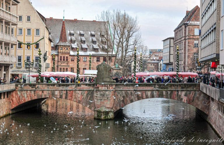 Puente del museo en Núremberg lleno de gente y decorado con puestos del mercado de navidad rojos y blancos