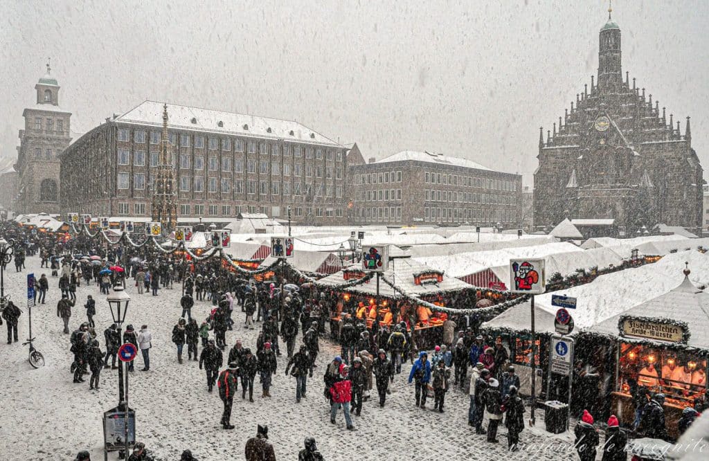 Gente visitando el mercado de navidad en la plaza principal de Núremberg mientras nieva