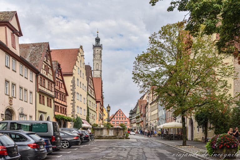 Herrngasse con coches aparcados junto a la fuente de piedra y la torre del ayuntamiento al fondo en Rothenburg ob der Tauber