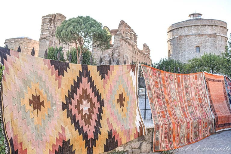 Alfombras de colores anaranjados colgando frente a las ruinas de la Basílica Roja en Bergama