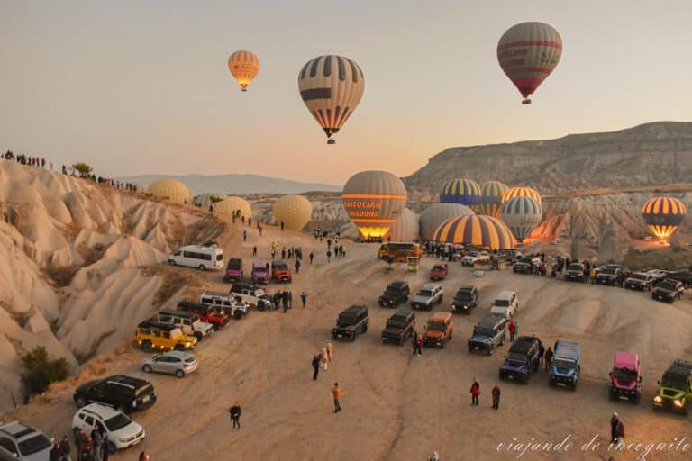 Muchos coches y mucha gente viendo como van despegando los globos al amanecer