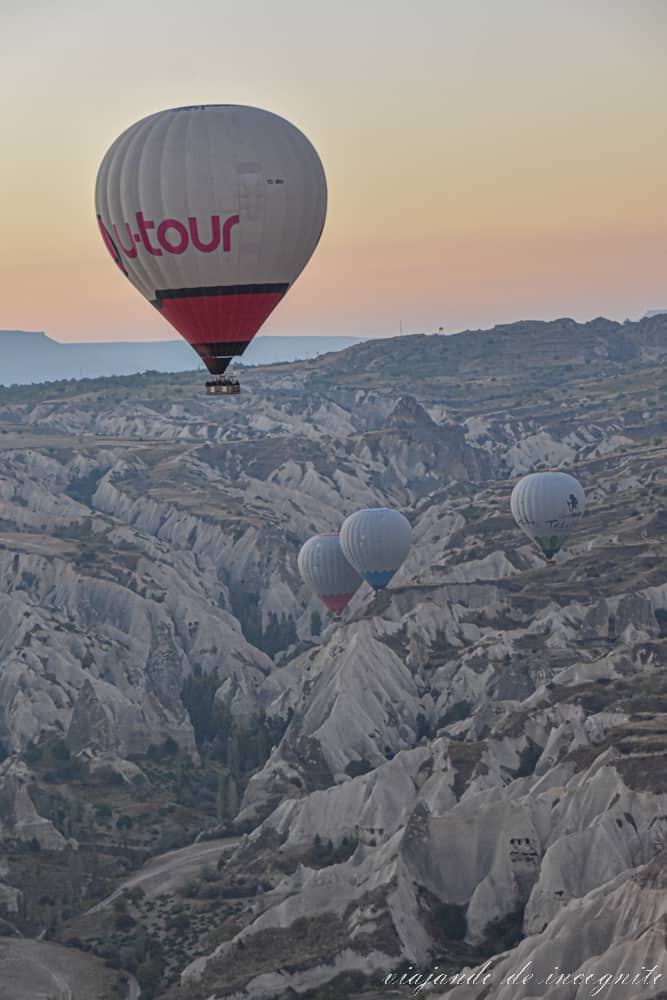 Globo blanco y rojo volando al amanecer sobre las formaciones rocosas de Capadocia con otros tres globos volando más abajo
