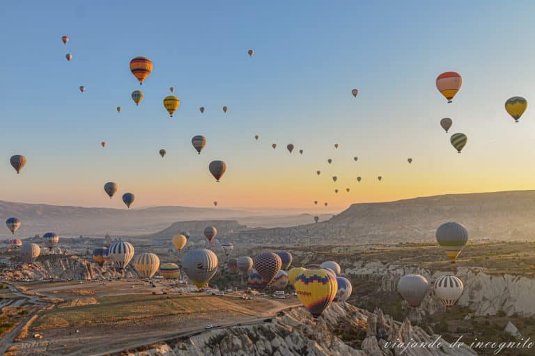 Muchos globos volando al amanecer en la Capadocia mientras en el suelo se ven coches de la gente disfrutando el espectáculo