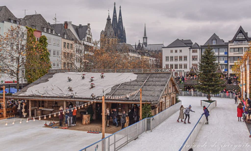 Gente patinando en la Pista de patinaje del mercado de navidad de la parte antigua de Colonia con catedral y el ayuntamiento en el fondo