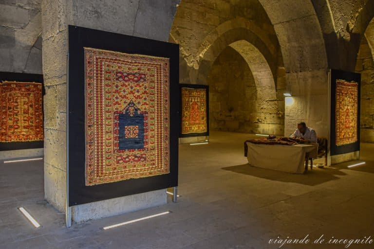 Hombre arreglando alfombras antiguas en una sala cuyas columnas están decoradas con alfombras en el Caravanserai de Sultanhani