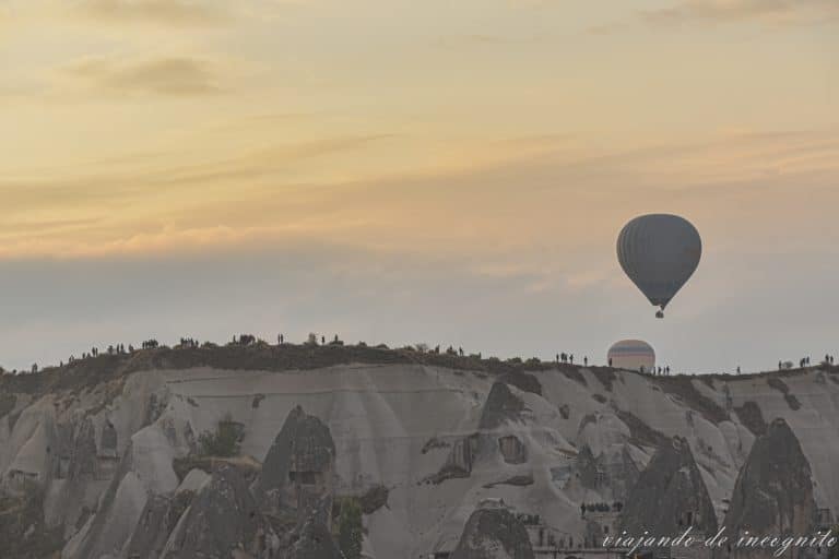 Dos globos volando al amanecer sobre muchos turistas viendo el espectáculo desde uno de los miradores