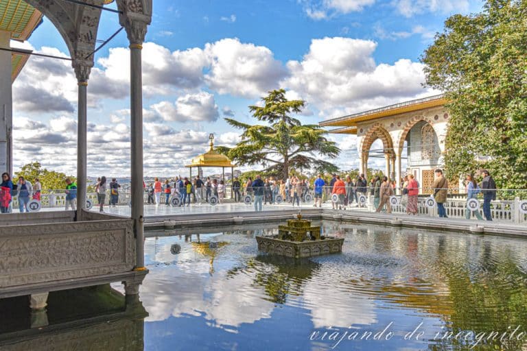 Mucha gente disfrutando de las vistas en una de las terrazas del Palacio Topkapi con un estanque donde se refleja las nubes y decorado con una fuente