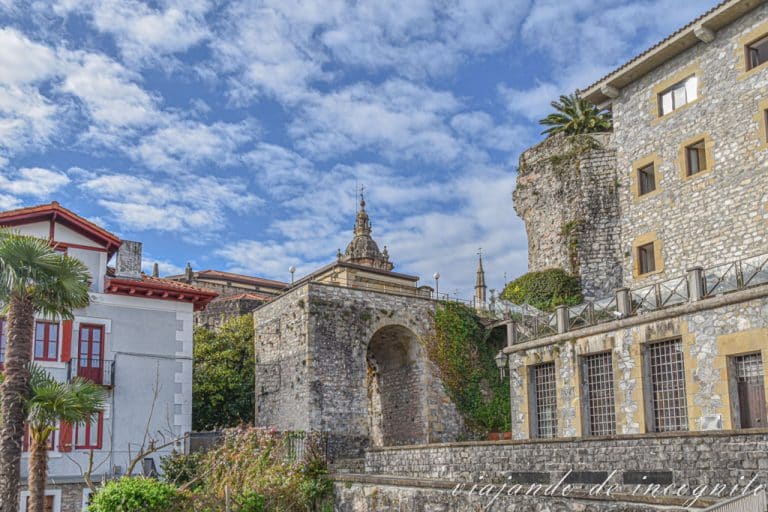 Restos de muralla y torre de iglesia contra un cielo azul y blanco.