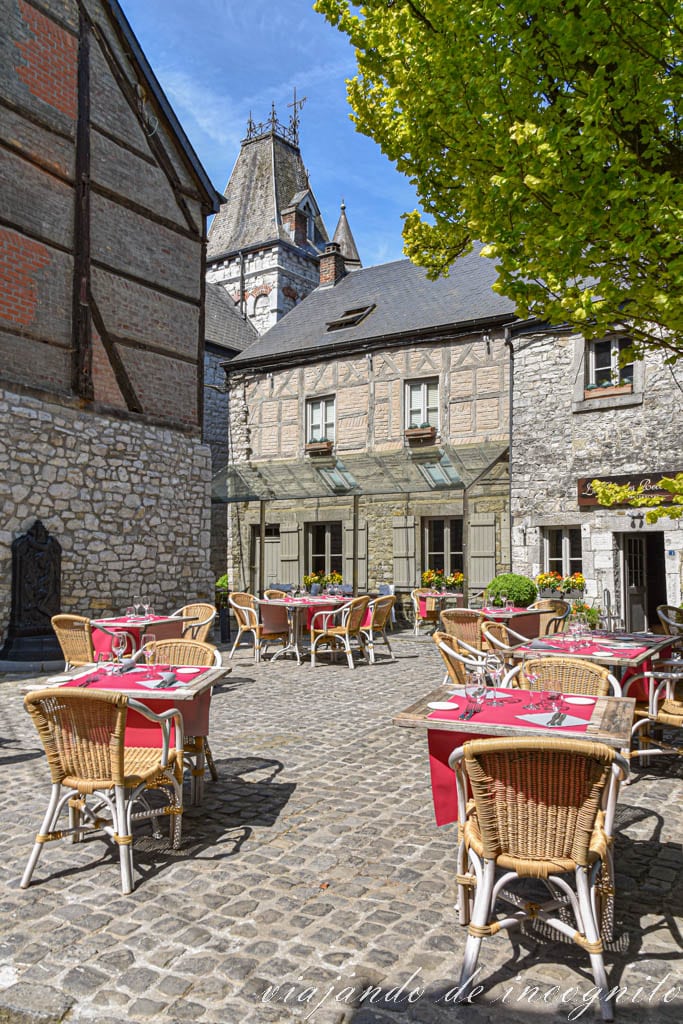 Mesas de restaurante con mantel rojo en una plaza de Durbuy rodeada de casas de piedra