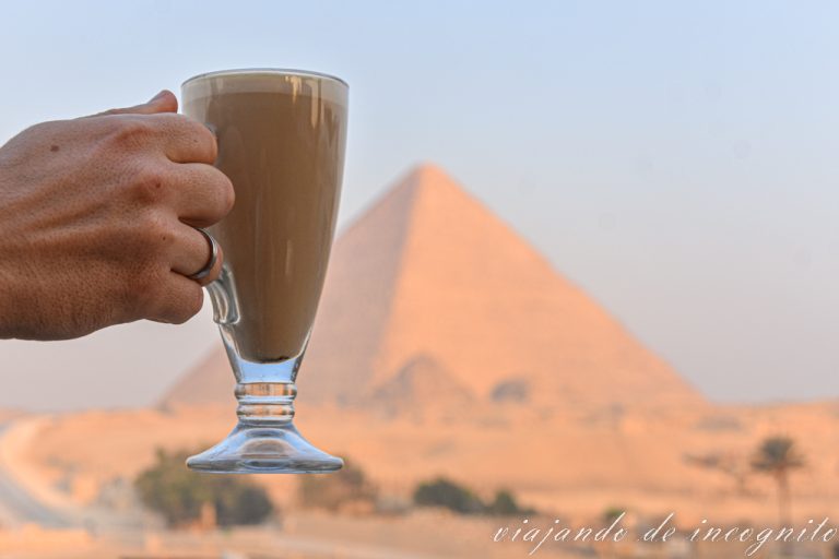 Mano sujetando vaso de café con la pirámide de Keops de fondo