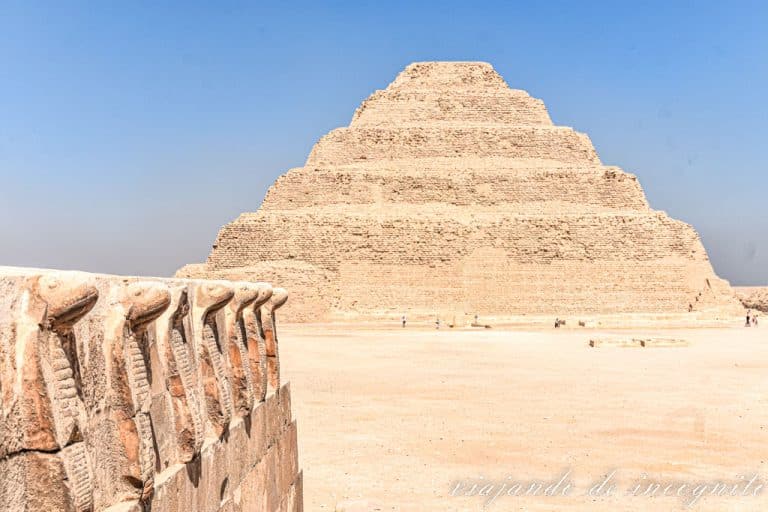 Fila de cobras esculpidas en piedra con la pirámide de Zoser al fondo