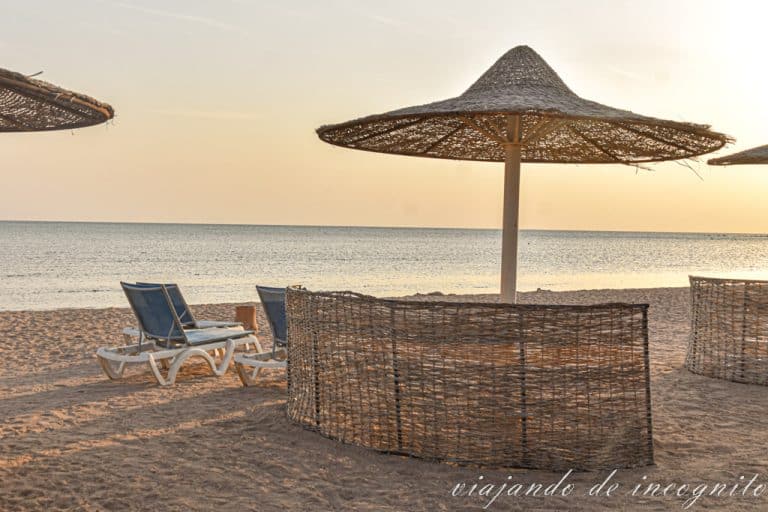 Playa en Hurghada con sombrilla y dos tumbonas protegidas por una pared de paja al atardecer