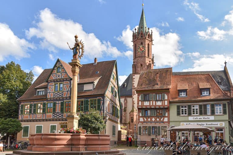Plaza de Ladenburg con la torre de la iglesia de fondo, casas de entramado de madera y una fuente decorada con una columna coronada con una estatua de la Virgen