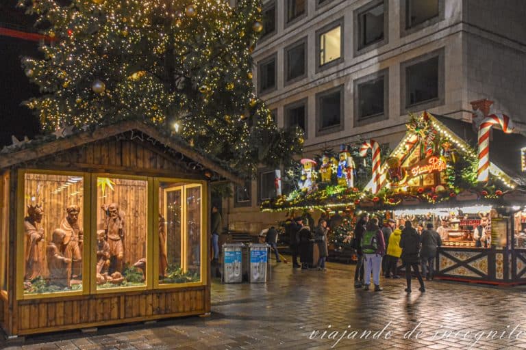 Puestos del mercado en la plaza del ayuntamiento bellamente decorados junto a un gran árbol de navidad iluminado y un nacimiento de madera de gran tamaño
