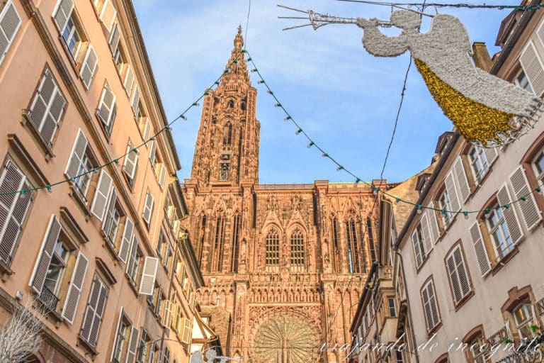 Vista de la parte superior de la catedral de estrasburgo enmarcada por las casas de la calle de enfrente y ángeles decorativos de navidad