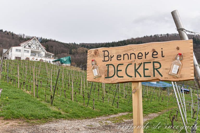 Cartel de la destilería Decker con el edificio y los viñedos al fondo. Uno de los lugares que ver en Sasbachwalden