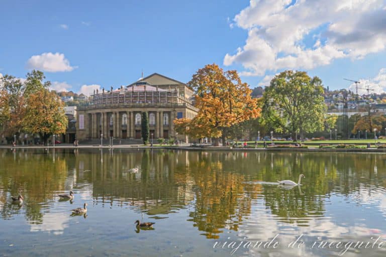 La Ópera reflejada en el agua del estanque, donde hay patos, y rodeada por árboles con colores otoñales.
