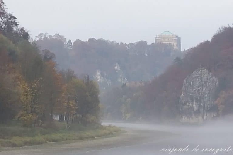 El Danubio cubierto de niebla y rodeado de árboles con colores otoñales. En lo alto puede verse el Befreiungshalle de Kelheim