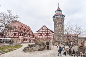 Gente entrando en el castillo imperial de Núremberg, con la torre Sinnwell y la casita de entramado de madera donde se encuentra el pozo profundo