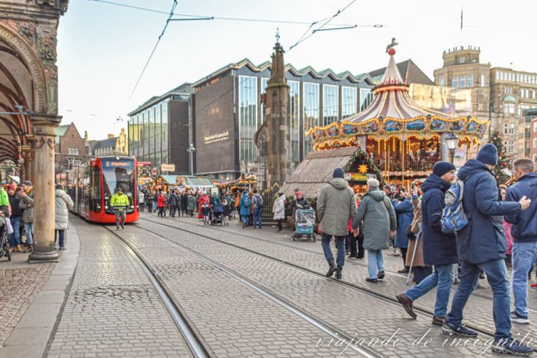 Un tranvía circula frente al ayuntamiento de Bremen durante el mercado de navidad. Hay tanta gente que un hombre ke abre el camino tocando campanas.