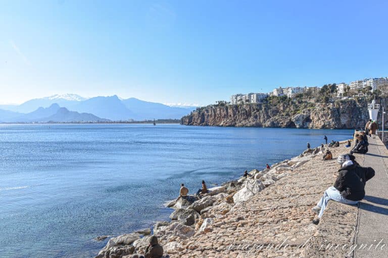 Muchas personas están sentadas en las rocas junto al faro en el puerto de Antalya