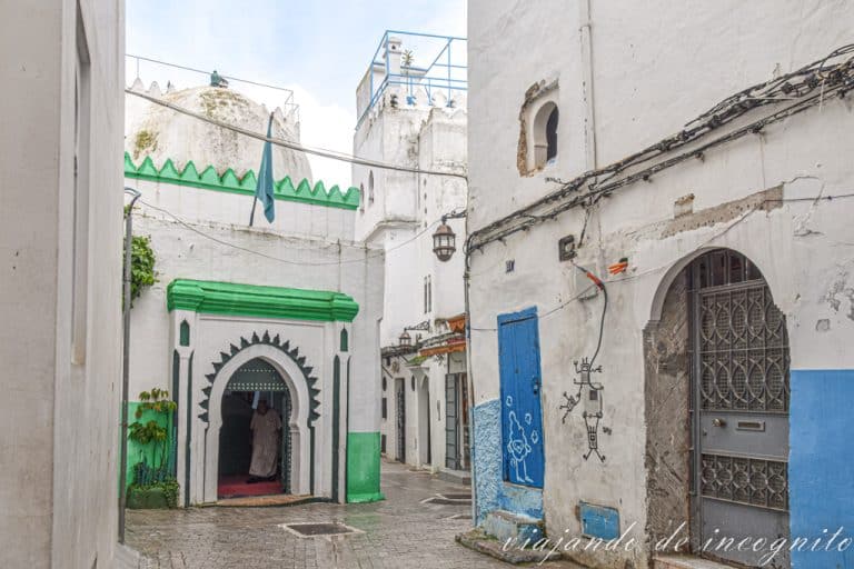 Una de las calles blancas de la Kasbah de Tánger donde hay una casa decorada en azul y una pequeña tumba decorada en verde.