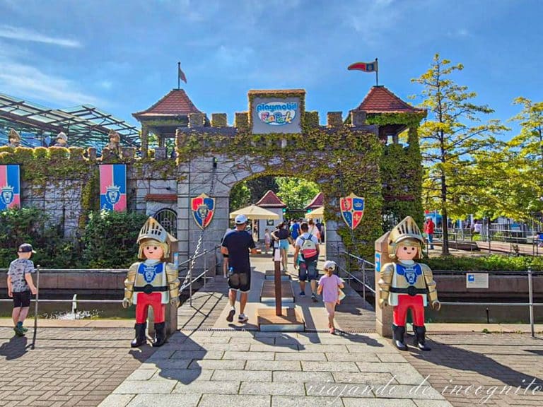 Varias personas entran al Playmobil Funpark, cuya entrada tiene forma de castillo y está defendida por dos muñecos playmobil con forma de caballero de gran tamaño.