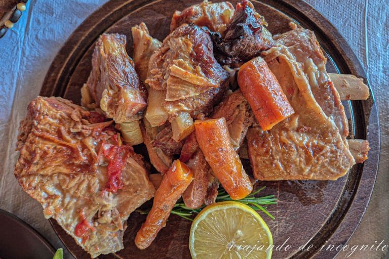 Plato de parrillada de carne de cordero acompañada de zanahoria cocida y rodajas de limón.