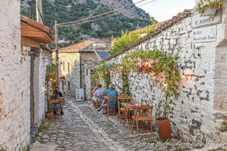 Cuatro personas sentadas en pequeñas mesas de madera de una terraza de uno de los restaurantes de Gorica al atardecer, Berat