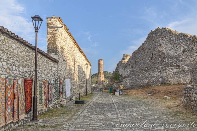 Una de las calles del castillo de Berat decorada con alfombras y con un vendedor de fruta. Al fondo se ve el minarete de la mezquita Roja.