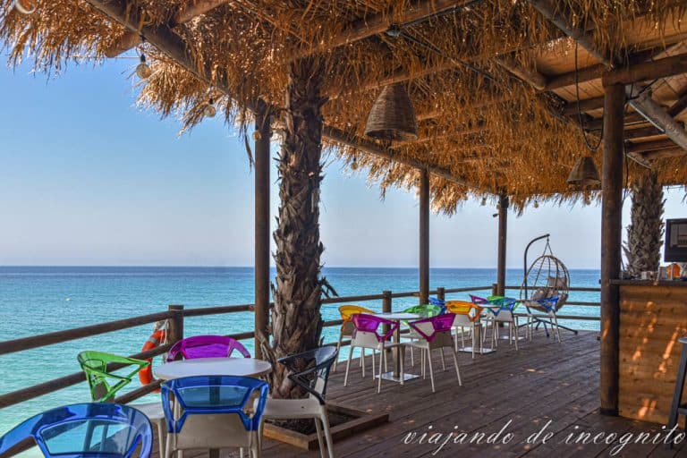 Mesas del restaurante la Onda en la playa Lukova con sillas de colores. Al fondo de ve el mar.