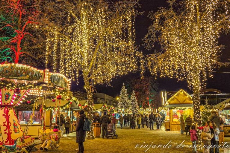 Gente bajo los árboles iluminados del mercadillo navideño de Charlottenburg y junto a un carrusel.