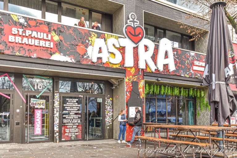 Dos personas hablan frente a la puerta de la cervecería Astra en St Pauli, que está cerrada. SObre ella hay un balcón donde hay otras dos personas.