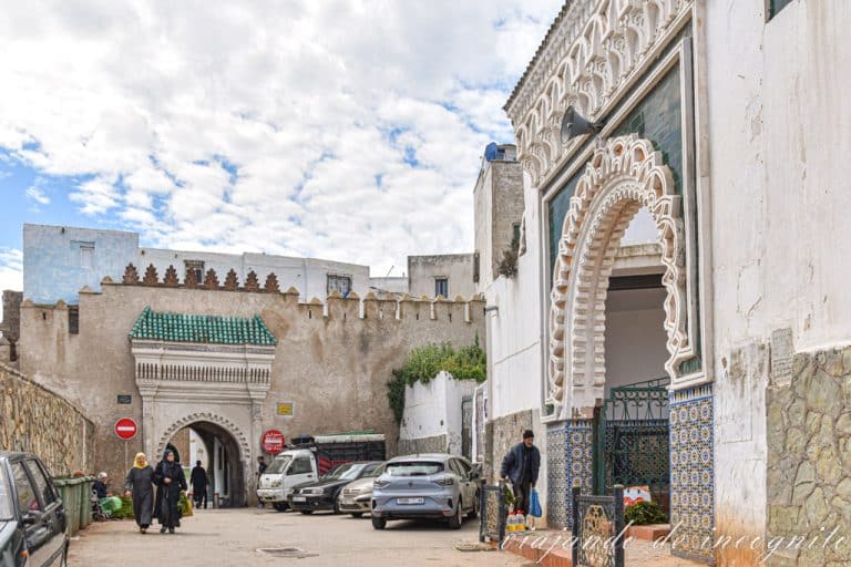 Varias personas entran y salen por Bab Mkabar. Junto a la puerta hay varios coches aparcados.