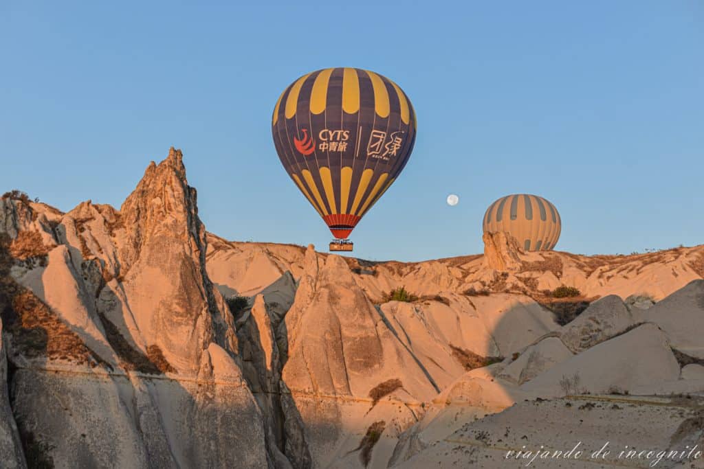 Dos globos volando junto a las formaciones rocosas de la Capadocia con la luna en el cielo