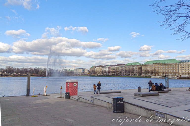 Unas pocas personas están en el Jungfernstieg frente al Alster Interior, donde funciona la fuente.