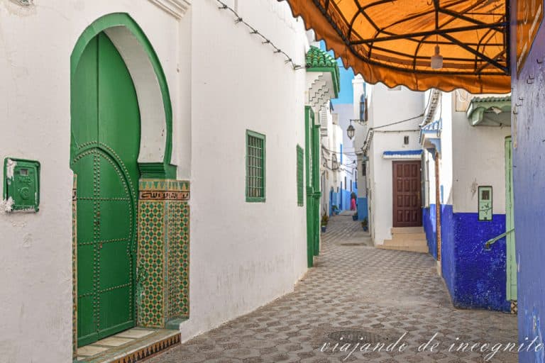Calle blanca de la Medina de Asilah con puertas verdes y zócalo azul.
