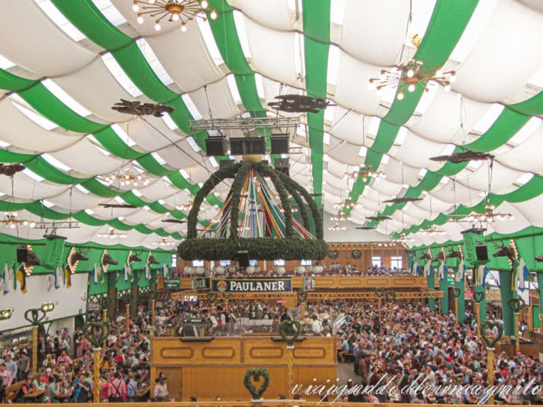 Muchas personas celebran la Oktoberfest dentro de una carpa decorada con los colores blanco y verde.