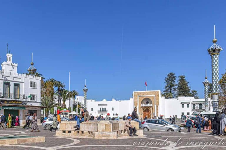 Varias personas están sentadas sobre bloques de piedras en la plaza Hasan II frente al Palacio Real.