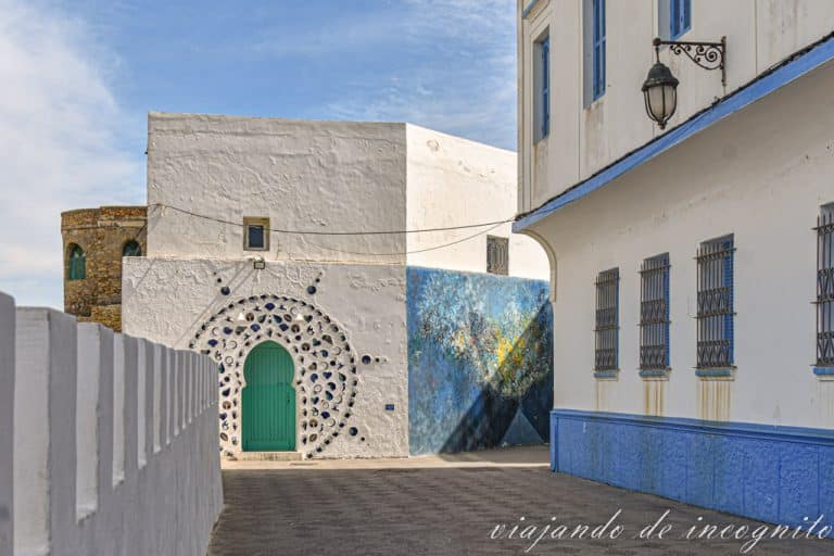 Puerta verde decorada con un circulo en donde hay relieves de manos, pájaros, conchas, corazones y otros elementos decorativos.