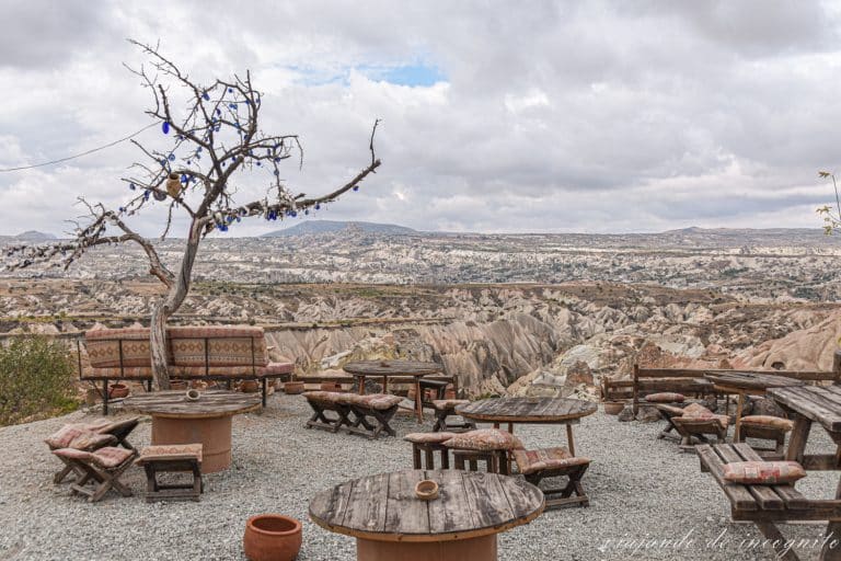 Terraza con mesas y bancos de madera con cojines con vistas al Valle Rojo y junto a un árbol seco decorado con ojos de Fátima