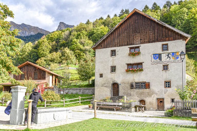 Dos personas se encuentran junto a la fuente frente al ayuntamiento y los establos de la casa de Heidi en Suiza.