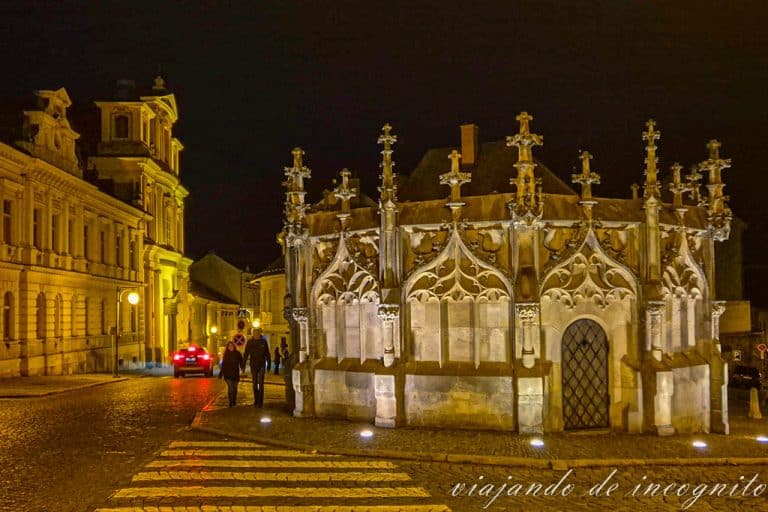 Una pareja pasea junto a la fuente de piedra de Kutná Hora al anochecer.