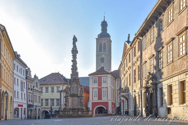 Espacio de Kutná Hora pronto por la mañana donde está la columna de la plaga. Su sombra tapa la fachada renacentista de una de las casas. Al fondo sobresale la torre de la iglesia de Santiago.