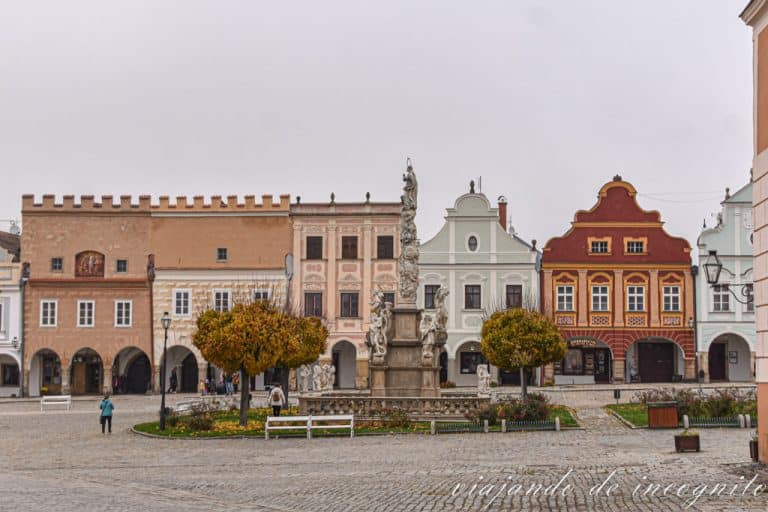 Vista de uno de los laterales de la plaza de Telc. Se ve la columna de la Pesta y al fondo tres casas con hastiales en distintos tonos pastel.