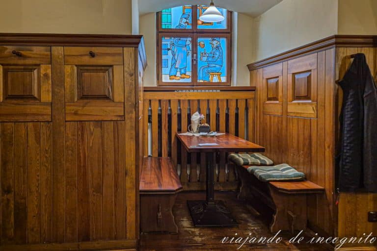 Mesa de madera bajo una ventana decorada con una imagen del soldado Sevjk en el restaurante Sevjk de Telc.