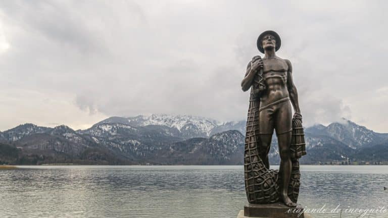 Estatua del pescador de Kochel frente al lago en invierno con los montes nevados al fondo.