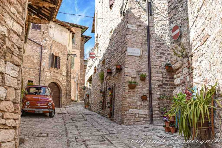 Una calle de Spello decorada con flores donde hay aparcado un Fiat de color rojo.