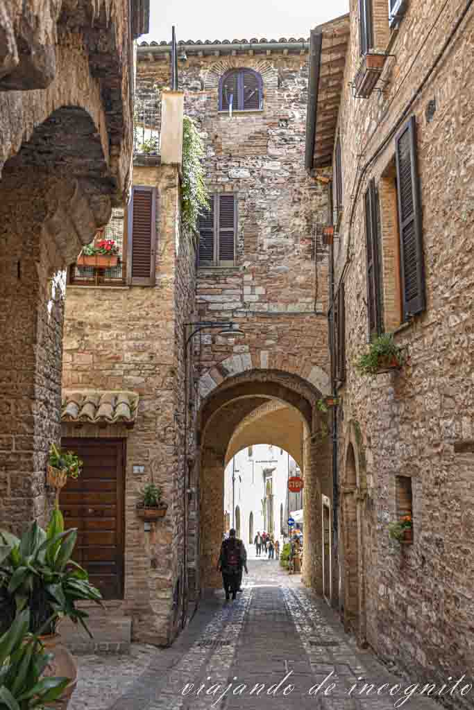 Un señor camina bajo un arco en la calle principal de Spello